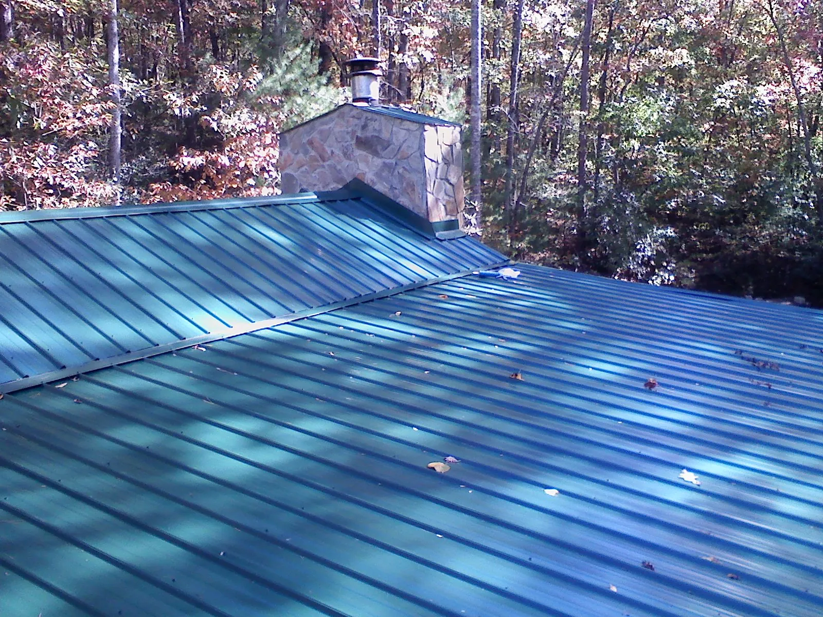 New green metal roof and stone chimney surrounded by autumn woods in Bridgewater