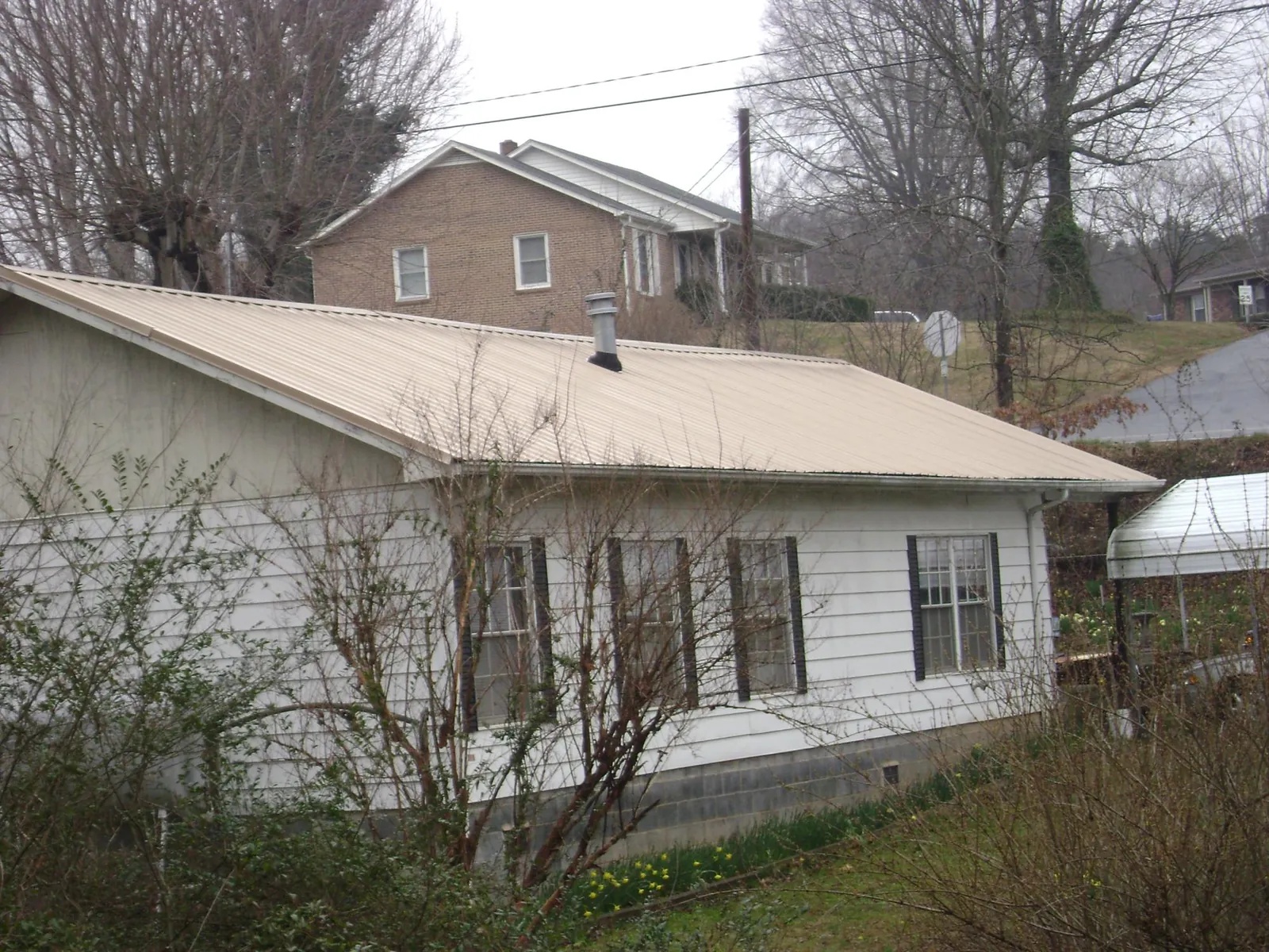 Tan metal roof on a white sided house set into a hillside — Commercial Roofing by Roofing Brothers in Bridgewater